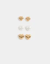 Set de tres pares de aros pasantes con forma de corazón: un par dorado con strass, un par blanco símil perla y un par dorado liso.