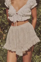 Top crop blanco de escote cuadrado y manga corta abullonada. Detalle de lazada en el pecho y volantes en el escote y el bajo.