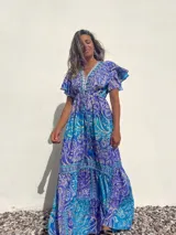 Vestido largo de seda con estampado paisley en tonos turquesa, azul y blanco. Tiene escote en V, mangas cortas con volados y talle imperio con cordón ajustable.