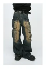 Pantalón de jean ancho (baggy) con lavado oscuro y efecto desgastado en tonos marrones/ocre. Presenta múltiples bolsillos cargo grandes con tapa y botones a presión en las piernas.