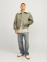 Campera bomber color verde oliva, de manga larga y cuello extendido. Tiene puños ribeteados, cierre con cremallera, bolsillo en la manga y bolsillos frontales con cierre de botón.