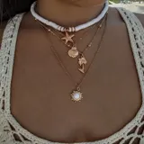 Set de cuatro collares dorados de diferentes largos. El primero es un choker de cuentas blancas, el segundo tiene un dije de estrella de mar, el tercero tiene un dije de caracol y un dije de palmera, y el cuarto tiene un dije de sol con una piedra blanca en el centro.