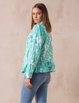Campera blanca con bordado floral en verde agua, cuello solapa, cierre con botones, bolsillos delanteros y ruedo fruncido.