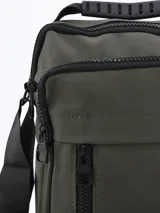 Bandolera verde militar con correa ajustable negra, cierre superior y bolsillos frontales con cremallera.