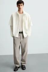 Pantalón de vestir color blanco hueso, de corte recto y tiro medio, con cintura elástica y cierre frontal de botón y cremallera. Presenta bolsillos frontales y bolsillos traseros de vivo.