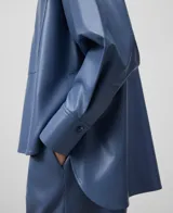 Sobrecamisa azul de cuero sintético con cuello mao, cierre frontal con botones, bolsillo de parche en el pecho, mangas largas y corte asimétrico.