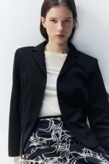 Blazer negro de punto pesado con solapas de muesca, corte entallado, hombreras, bolsillos delanteros ribeteados y abertura decorativa en los puños.