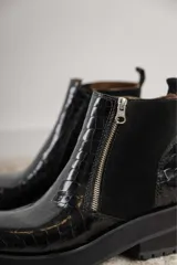 Botines negros de cuero con caña baja, puntera redondeada y cierre frontal con cremallera. Presentan paneles laterales de gamuza y suela track con plataforma.