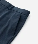 Pantalón de vestir gris claro con textura, de corte recto, con bolsillos laterales y traseros. Se ajusta a la cintura con cinturón de cuero negro.