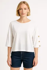 Remera blanca de corte holgado con mangas 3/4 y detalle de botones dorados en las mangas.