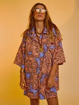 Camisa oversize de algodón con estampado abstracto en tonos marrón, naranja y celeste. Tiene cuello clásico, cierre frontal con botones y mangas cortas.