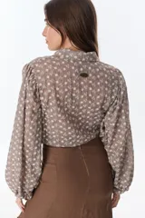 Camisa marrón con estampado de flores blancas, de corte cropped con nudo frontal y mangas largas abullonadas.