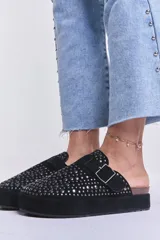 Zueco negro con plataforma, tachas plateadas y hebilla ajustable.