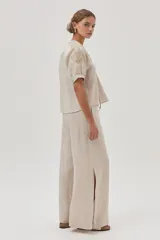 Blusa de lino color arena, de manga corta, con cuello redondo y lazo ajustable. Presenta bordados en las mangas y el escote.