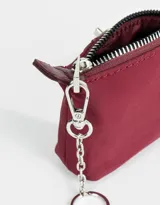 Monedero color verde claro de tela deportiva con solapa con broche con botón, cierre superior con mosquetón y tag en relieve.