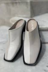 Zuecos color beige confeccionados en cuero vacuno, con punta cuadrada y suela plana color negro.