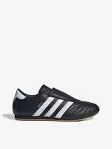 Zapatillas Adidas Taekwondo negras de cuero, sin cordones y con las tres tiras blancas en los laterales.