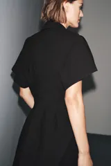 Vestido midi de algodón color negro, con cuello solapa, manga corta y falda evasé. Cierre frontal con botones y lateral con cremallera oculta.