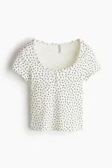 Remera blanca con estampado de flores pequeñas en negro, escote cuadrado y tapeta de botones. Corte entallado y mangas cortas.