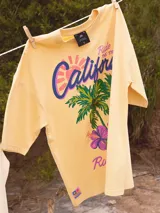 Remera color crudo de corte oversized con estampado de palmeras, flores y texto 'California' y 'Rusty Tribe'.