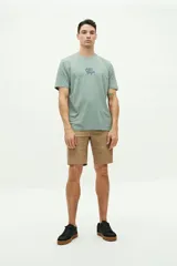 Remera verde de manga corta con cuello redondo y estampado en la espalda con la frase "Côte d'Azur Surfer avec les mouettes" y un dibujo de una sombrilla, una reposera y gaviotas.