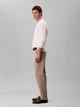 Pantalón chino de corte slim color beige, confeccionado en algodón y elastano. Presenta cierre con cremallera y botón, diseño clásico de cuatro bolsillos y logo de Calvin Klein bordado en la parte posterior.