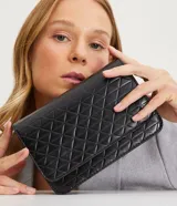 Bolso pequeño estructurado color negro, con textura capitoneada, asa de cadena y solapa frontal con botón a presión. Incluye divisor interno con cremallera.