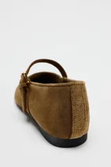 Zapato plano tipo bailarina color marrón de serraje, con escote redondo y cierre mediante hebilla en el empeine.