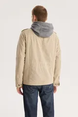 Campera color beige con capucha gris, cierre frontal con cremallera y botones a presión, cuatro bolsillos frontales con solapa y charreteras en los hombros.
