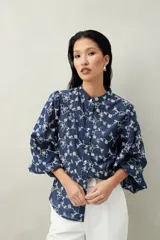 Camisa azul con bordado floral blanco, cuello mao, abotonadura frontal y mangas largas abullonadas.