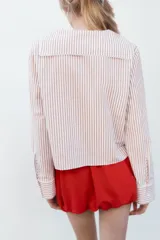 Camisa de popelina a rayas marrones y blancas, con cuello bobo con puntilla y escote pico con lazada. Manga larga con puño y cierre frontal con botones.