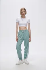Pantalón de jogging color celeste con cintura elástica ajustable con cordón y puños elásticos. Presenta tres tiras verticales blancas en la parte inferior de la pierna.