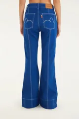 Pantalón de jean azul con corte amplio y fluido, cintura alta, cierre de cremallera y diseño acampanado. Presenta costuras blancas a contraste.