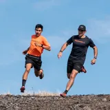 Remera deportiva naranja de poliéster y spandex, con logo Merrell estampado en el pecho.