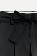 Pantalón negro de tiro alto con trabillas, bolsillos laterales y falsos bolsillos de vivo en la espalda. Incluye cinturón lazada en el mismo tejido.