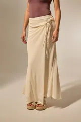 Falda larga de color natural, con diseño envolvente y detalle de anudado lateral en la cintura. Presenta una caída fluida y ligera.