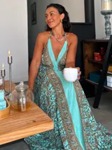 Vestido largo tipo solera, color turquesa con estampado paisley en tonos marrones y dorados. Diseño con escote halter anudado al cuello y abertura frontal central en color liso.