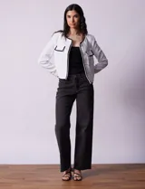 Chaqueta de tweed blanca con ribete negro, escote a la base, abertura central con botones, bolsillos delanteros y puños con aplique de botones perlados.