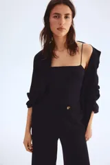 Pantalón sastrero tobillero negro de tiro alto con cierre y pretina prolongada con botón. Presenta bolsillos al bies, bolsillos traseros decorativos y piernas amplias con pliegues adelante y atrás.