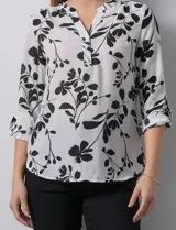Blusa de gasa blanca con estampado floral en negro. Presenta cuello a la base con escote en V y abertura con botones. Las mangas son largas y se pueden ajustar a tres cuartos.