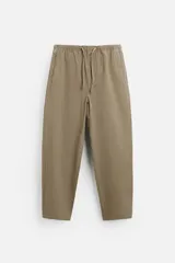 Pantalón color arena de corte carrot fit, confeccionado en tejido de algodón. Tiene cintura elástica ajustable con cordón, bolsillos frontales y un bolsillo trasero de plastrón.