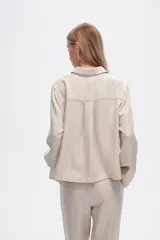 Camisa color natural de poliéster con cuello camisero, cierre con botones, dos bolsillos frontales y corte ancho.