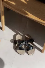 Sandalias bajas de cuero color beige con doble tira de cuero negro con textura y hebilla metálica.