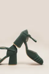 Zapato de tacón de terciopelo verde con correa al tobillo, punta redondeada y tacón cuadrado.