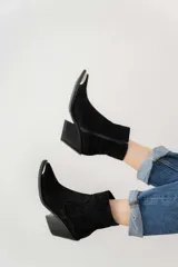 Bota corta de cuero gamuzado color marrón oscuro, con punta fina y detalle metálico. Tiene cierre lateral y taco de madera.