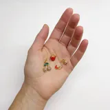 Gargantilla de cuentas facetadas color borgoña con cierre de mosquetón dorado y cadena de alargue. Incluye cuatro dijes colgantes dorados: cerezas con strass rosa, frutilla roja, corazón rojo esmaltado y estrella con strass.