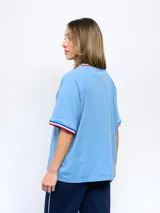 Remera blanca de corte clásico con cuello redondo y mangas cortas con puños tricolor (azul, blanco y rojo). Presenta el logo de Umbro bordado en el pecho izquierdo y el escudo del Club Nacional de Football bordado en el pecho derecho.