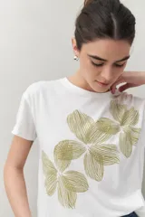 Remera blanca de manga corta con estampado floral en tonos dorados en el frente.