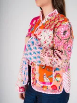 Chaqueta con cuello alto y botones tipo nudo, confeccionada con la técnica patchwork, combinando retazos de telas tradicionales con bordados y estampados vibrantes que mezclan flores, formas geométricas y cultura textil.