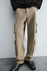 Pantalón de denim color beige, corte relaxed fit, con bolsillos laterales tipo cargo con solapa y cierre de botón. Cierre frontal con botón y cremallera.